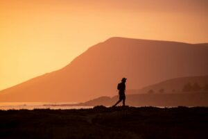 man walking at dusk in front of a hilly landscape
