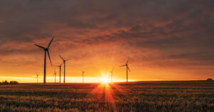 a field of windmills with a setting sun landscape behind them
