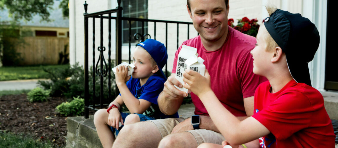 Father and two sons sitting on a porch drinking water