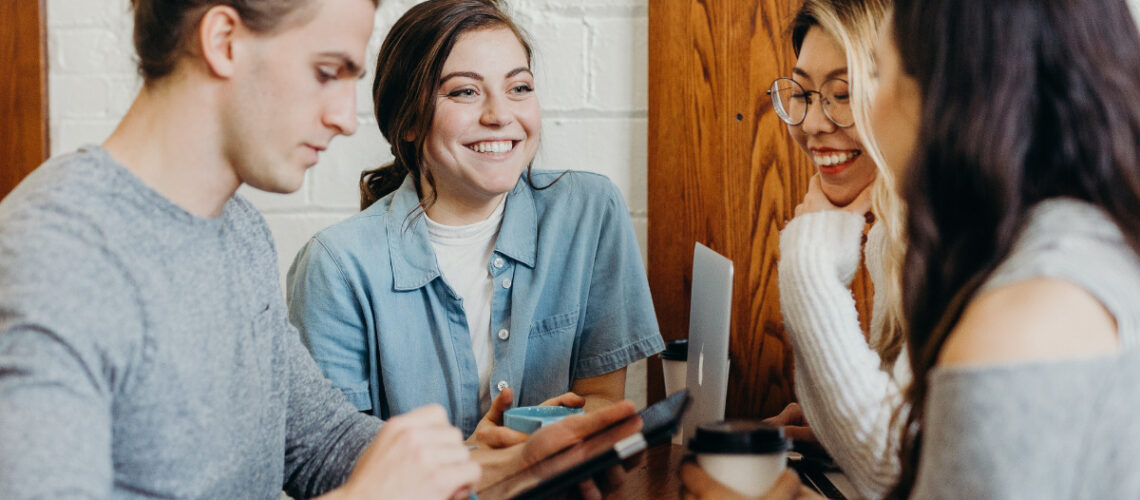 4 students talking and laughing sitting at a table