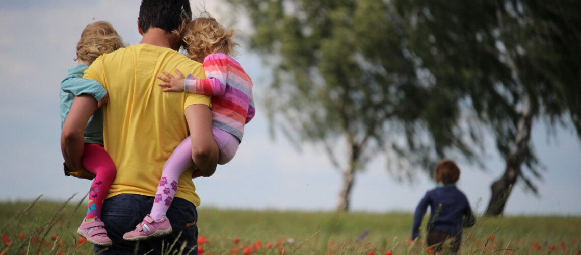 a father walking through a field with his three children