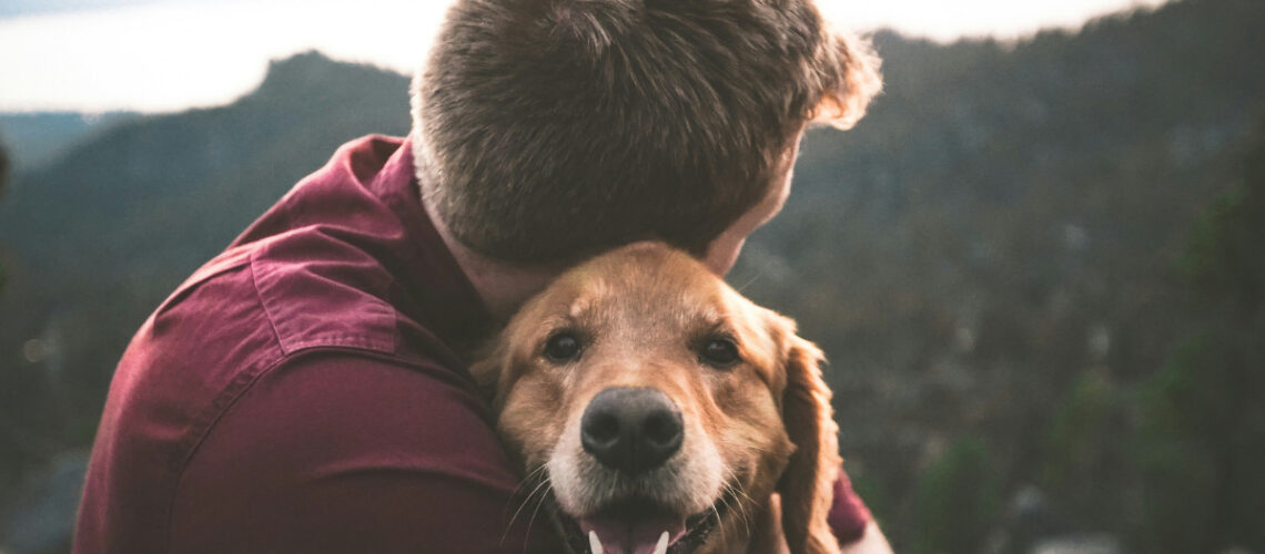 man in red sweater hugging a dog outside