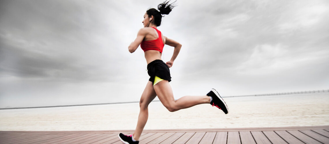 Young woman running on boardwalk in athletic gear.