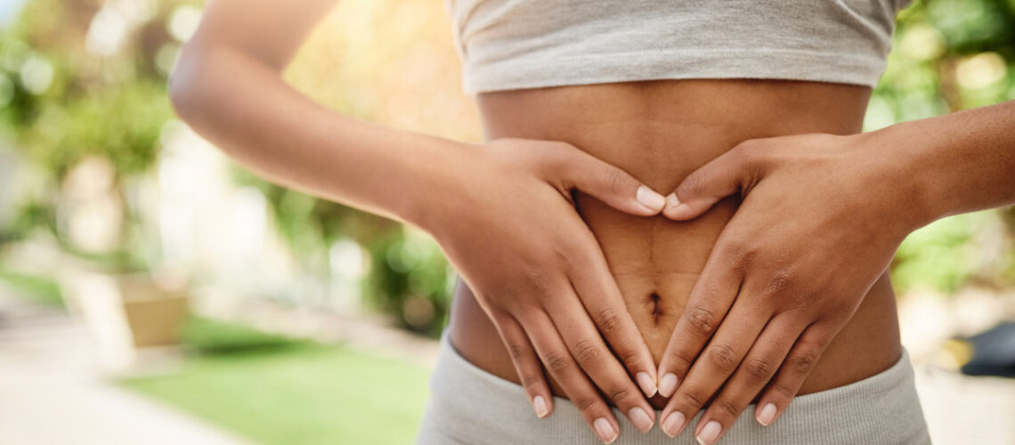 Young woman in athletic gear holding her hands on her stomach in the shape of a heart.