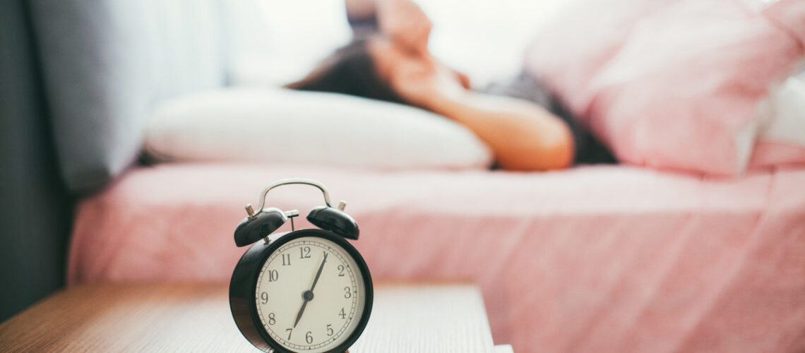 Individual waking up from sleeping next to an alarm clock.