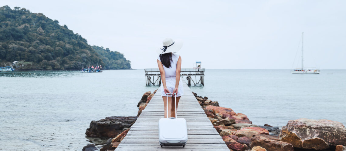 Young woman pulling a white suitcase on a dock.