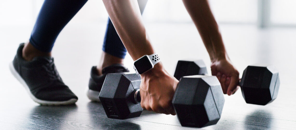 Image demonstrating building muscle. Young athletic individual picking up body weights about to exercise.