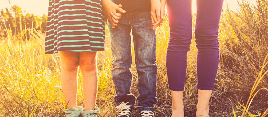 Three siblings holding hands in a field