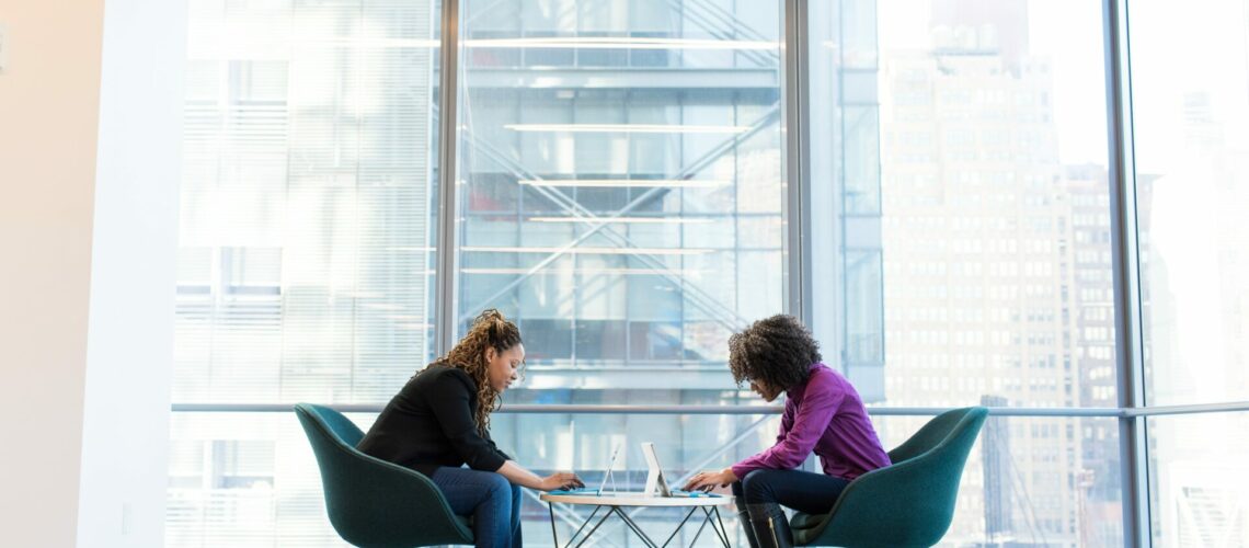 Two people working together sitting at a small table in front of windows