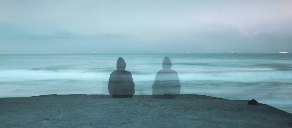 Someone sitting on a ledge in front of the ocean beside a transparent version of themself