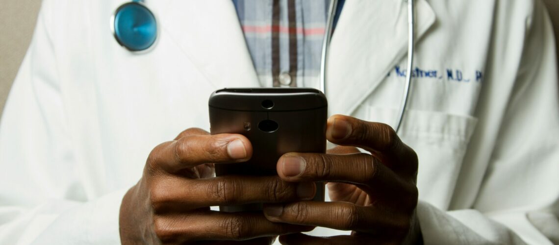 person wearing lavatory gown with green stethoscope on neck using phone while standing