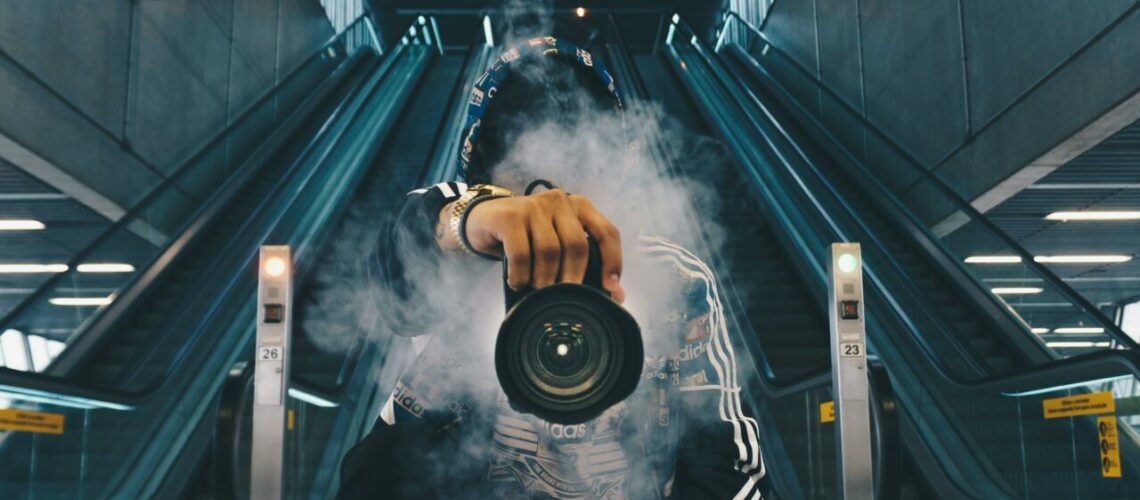 man with a camera obscured by smoke in front of escalators