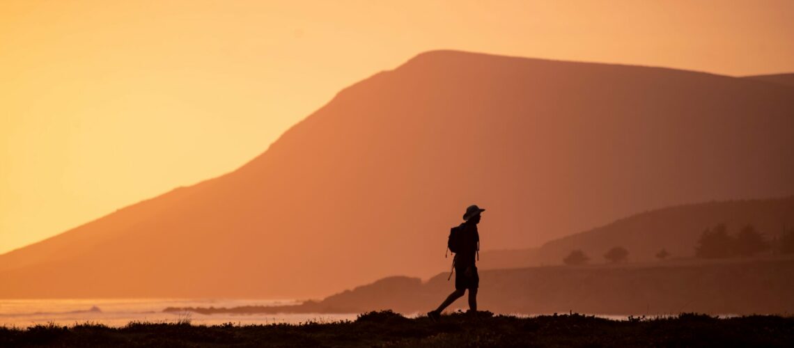 man walking at dusk in front of a hilly landscape